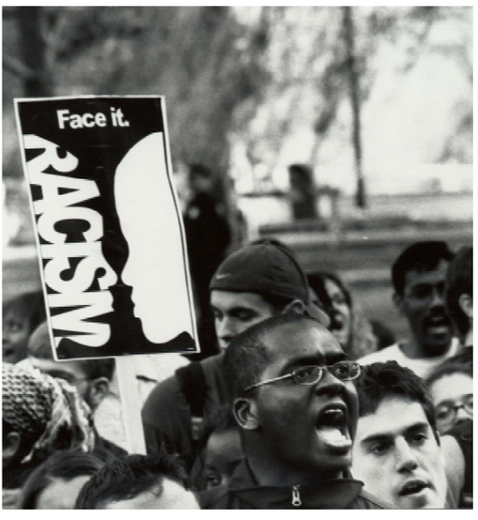 A young male protester holds a sign that reads "racism - face it."